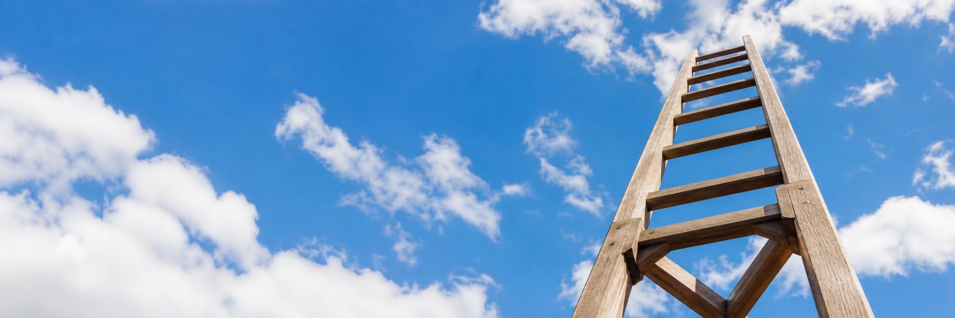 Wooden ladder reaching up into a bright blue sky with clouds